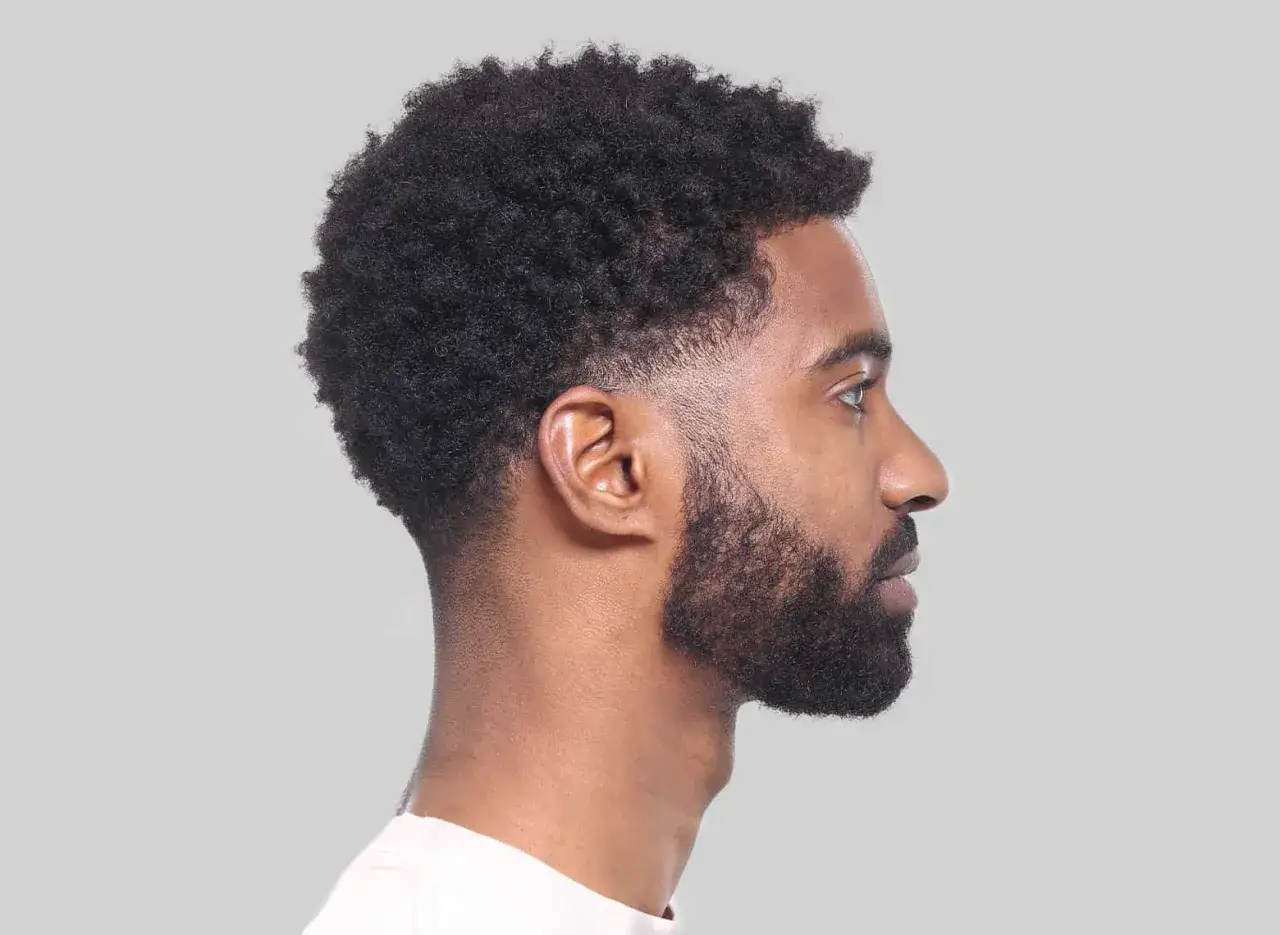 Perfil de hombre con cabello rizado y barba, luciendo un corte taper fade impecable en los laterales.