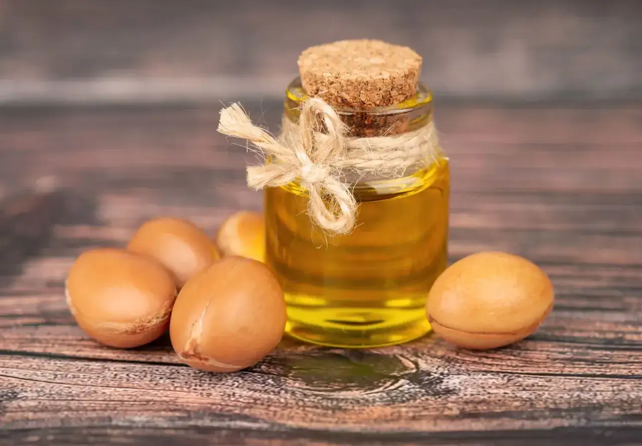 Aceite de arg&aacute;n para el pelo, en una botella r&uacute;stica con arganes alrededor.