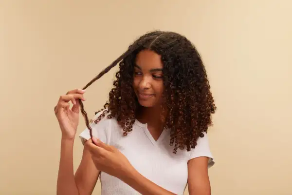 Chica con cabello rizado oscuro, aplicando el método curly a un mechón.