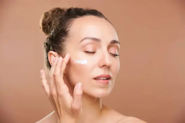 Mujer aplicándose crema en la mejilla, cuidando su piel con retinol en verano.