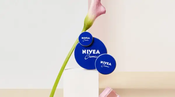 Tres latas de crema Nivea azul, con una flor rosa y verde, sobre un pedestal blanco.