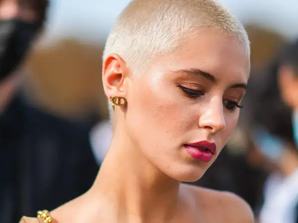Mujer con atrevidos rapado cortes de pelo corto, luce un maquillaje audaz y pendientes dorados.