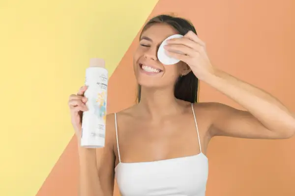 Mujer sonriente con agua micelar y disco desmaquillante, parte de su rutina limpieza facial.
