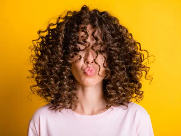 Chica con rizos perfectos, besando al aire. Su cabello luce espectacular gracias al método curlt.