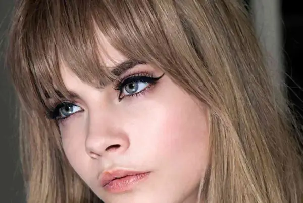 Primer plano de una mujer con flequillo recto y ojos maquillados con delineado cat eye. Explora los tipos de flequillo.