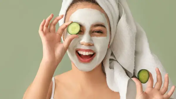Mujer sonriente con mascarilla facial y rodajas de pepino, disfrutando de tratamientos faciales naturales.