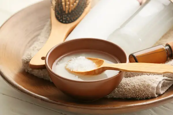 Un tazón con agua de arroz para la cara, una cuchara de madera con arroz, un cepillo para el cabello y botellas de productos de belleza.