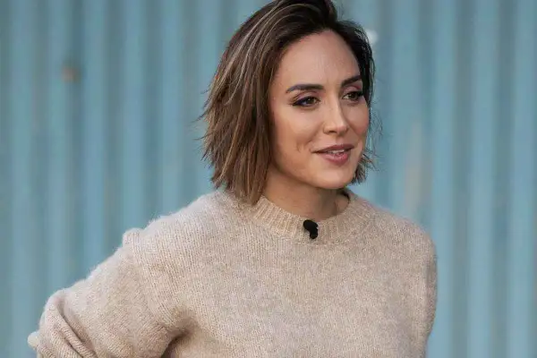 Mujer con un moderno corte bob con flequillo, luciendo un suéter beige y una sonrisa amable.