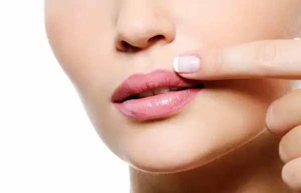 Dedo tocando labios rosados, notando pequeños granitos en los labios.