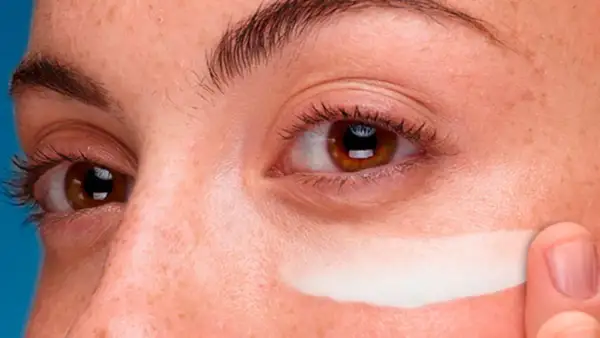 Dedo aplica crema contorno de ojos en toda la cara, cubriendo pecas y piel.
