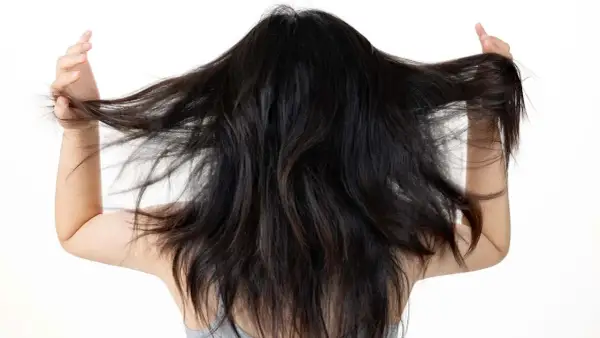 Mujer con cabello oscuro y largo, moviéndolo con las manos. Busca un alisado natural para domar su melena.