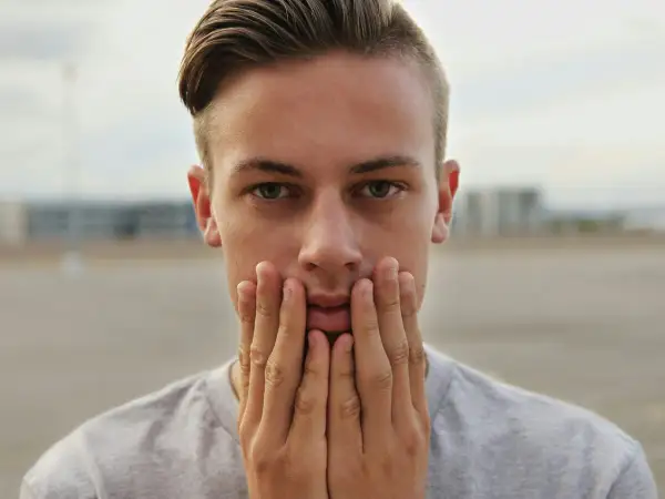 Primer plano de un joven con las manos en la cara, su peinado degradado resalta sus ojos verdes.