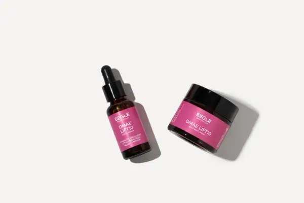 Un frasco de suero facial y un tarro de crema DMAE Lift10 de Segle, para una piel firme y redefinida.