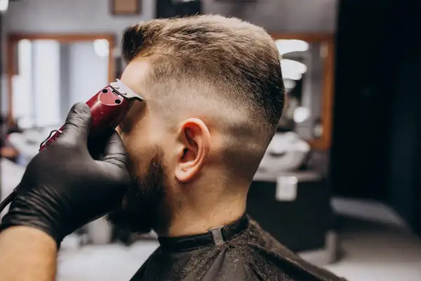 Barbero dando forma a un corte buzz cut fade con una máquina.