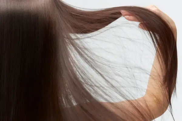 Cabello castaño oscuro y sedoso, con una mano acariciando las puntas. Descubre cómo cuidar el pelo fino para lograr este aspecto.