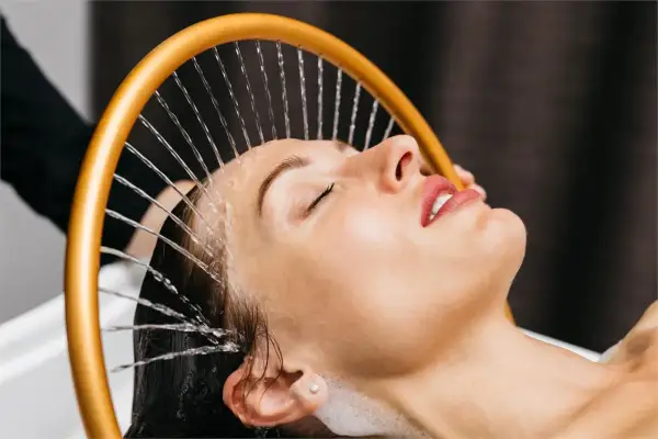 Mujer disfrutando de un relajante spa para cabello con agua cayendo sobre su rostro.