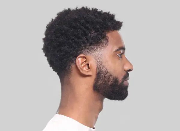 Perfil de hombre con cabello rizado y barba, luciendo un moderno corte taper fade.