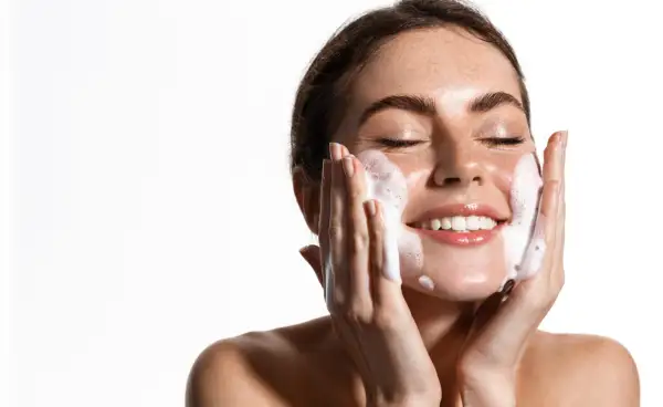 Una mujer sonríe mientras se realiza una limpieza facial noche con espuma.