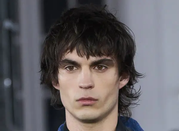 Hombre joven con un moderno mullet corto, cabello oscuro y despeinado, mirada intensa.