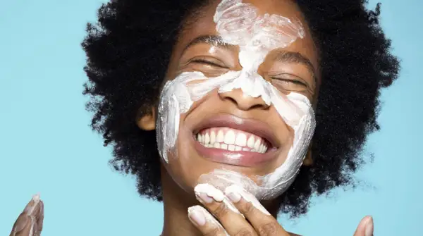 Una mujer sonríe con una mascarilla blanca en la cara. ¿Qué va primero el exfoliante o el limpiador?