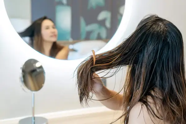Mujer revisando su cabello graso frente a un espejo, buscando remedios caseros para el cabello graso.