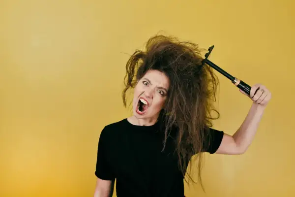Mujer frustrada con su pelo seco y encrespado, intentando peinarlo con un cepillo.