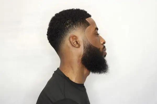 Hombre con un corte de pelo con tuper fade y barba cuidada, perfilado impecable.