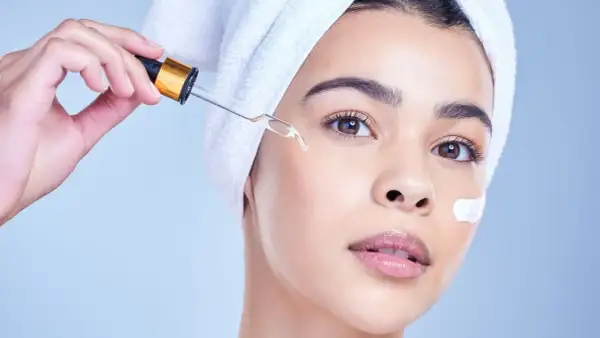Una mujer con toalla en la cabeza aplica un suero con gotero, ideal para usar niacinamida y retinol juntos.