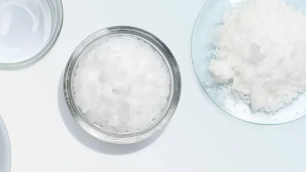 Botes con escamas blancas, como cetearyl alcohol, y un polvo blanco en un plato de vidrio.